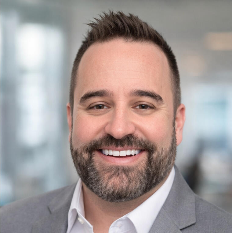headshot photo of Micah, from Micah Makes cents. Blurred background with his facial features in focus - smiling with a white collard shirt on under a taupe grey colored jacket.